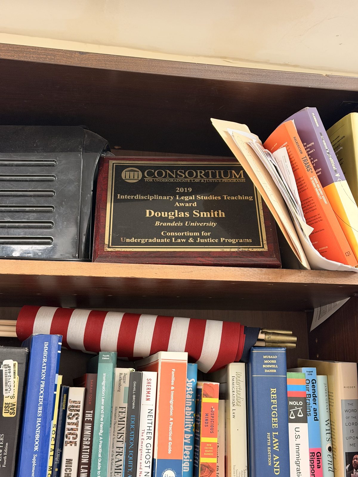 Immigration law books and a teaching award on an office bookshelf